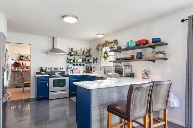 kitchen with dark wood-type flooring, stainless steel appliances, wall chimney range hood, blue cabinets, and kitchen peninsula