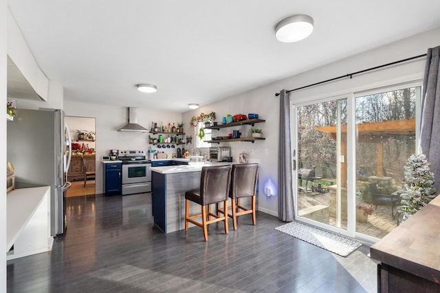 kitchen featuring wall chimney range hood, blue cabinets, a kitchen bar, kitchen peninsula, and stainless steel appliances