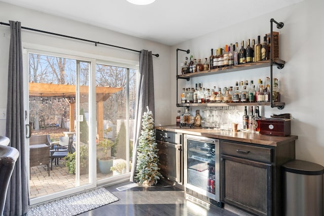 bar with dark brown cabinets, wood counters, dark wood-type flooring, and beverage cooler