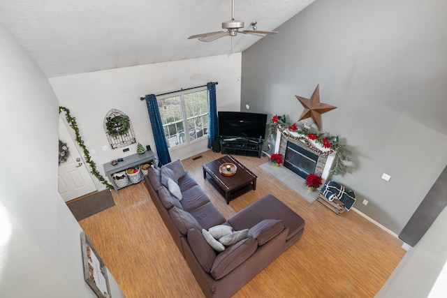 living room with a textured ceiling, vaulted ceiling, ceiling fan, a fireplace, and hardwood / wood-style floors