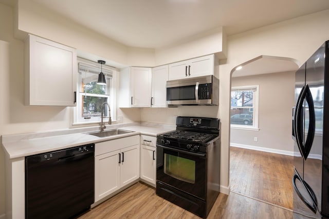 kitchen featuring sink, black appliances, decorative light fixtures, light hardwood / wood-style floors, and white cabinetry