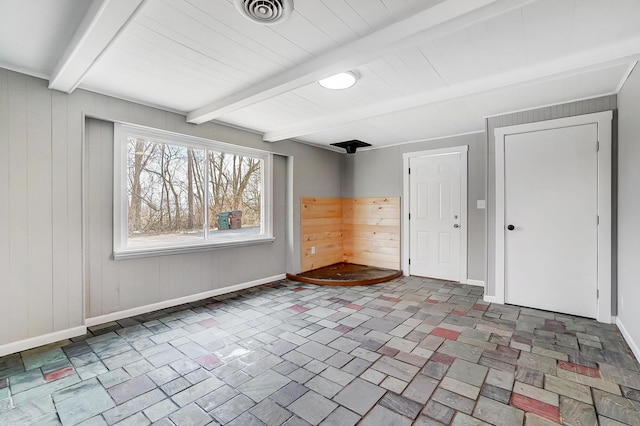 spare room with beam ceiling and wood walls