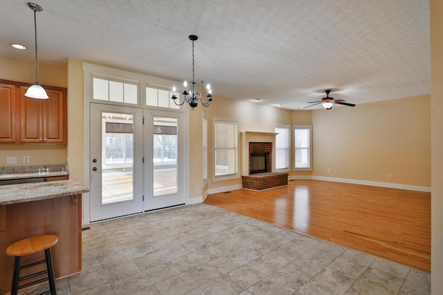 unfurnished living room with ceiling fan with notable chandelier, a textured ceiling, light hardwood / wood-style floors, and a fireplace