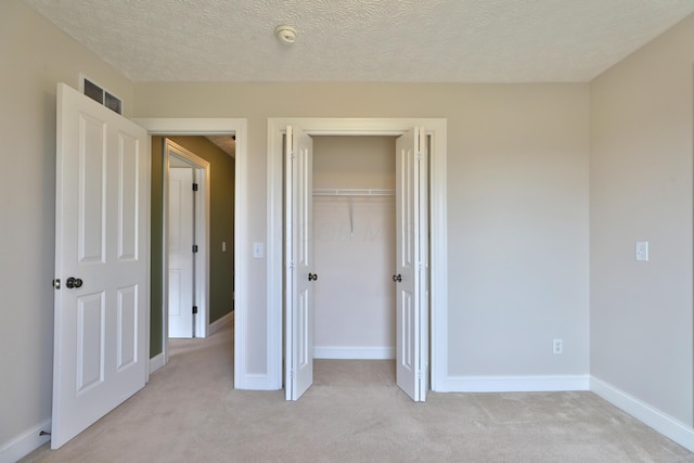 unfurnished bedroom featuring a textured ceiling, light carpet, and a closet