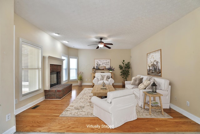 living room with ceiling fan, a fireplace, light wood-type flooring, and a textured ceiling