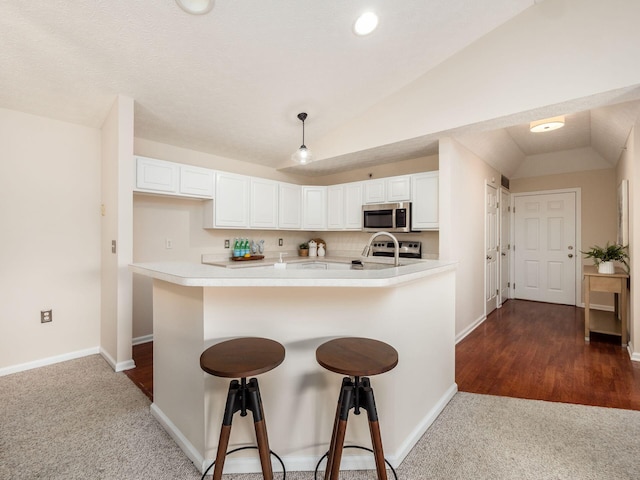 kitchen featuring a kitchen breakfast bar, white cabinetry, stainless steel appliances, and vaulted ceiling