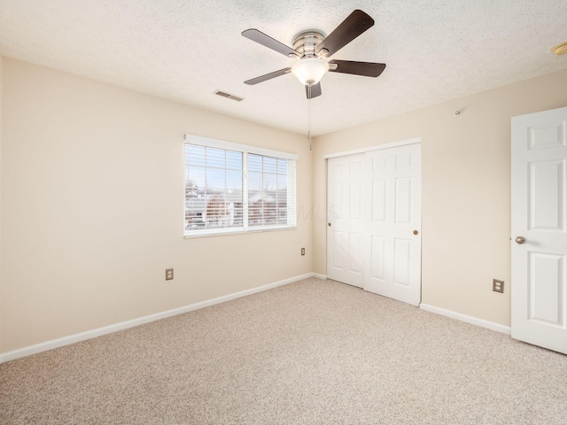 unfurnished bedroom with a textured ceiling, carpet floors, a closet, and ceiling fan