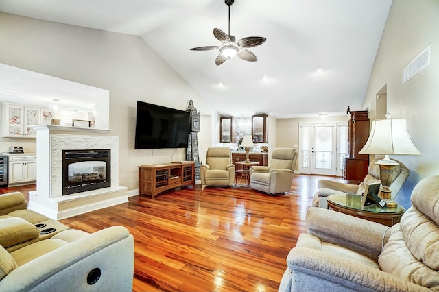 living room with ceiling fan, beverage cooler, high vaulted ceiling, light hardwood / wood-style floors, and a stone fireplace