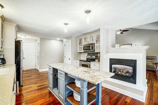 kitchen featuring light stone countertops, dark wood-type flooring, pendant lighting, decorative backsplash, and appliances with stainless steel finishes