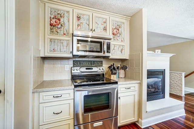 kitchen with cream cabinetry, decorative backsplash, stainless steel appliances, and dark wood-type flooring