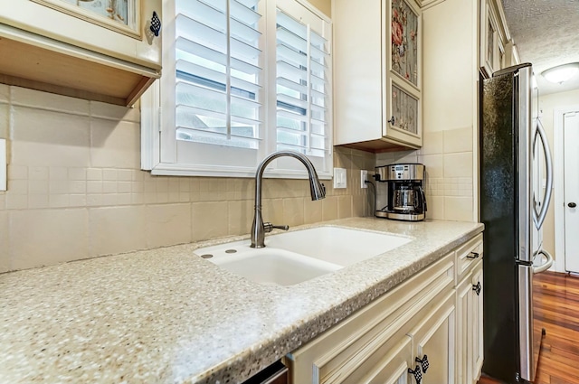 kitchen with backsplash, sink, stainless steel fridge, light stone counters, and wood-type flooring