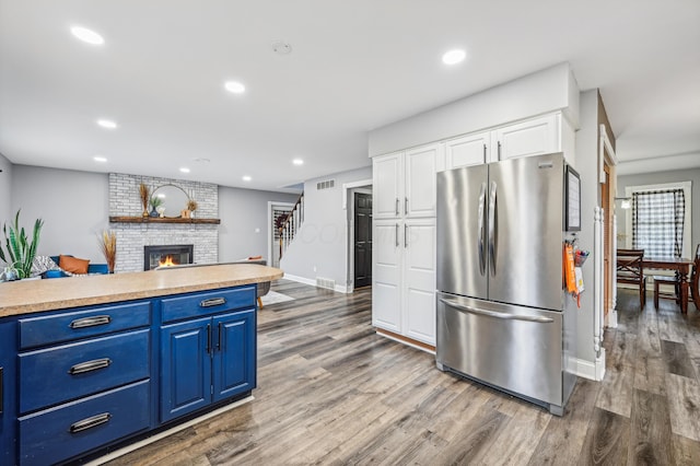 kitchen with a brick fireplace, stainless steel fridge, dark hardwood / wood-style floors, and blue cabinets