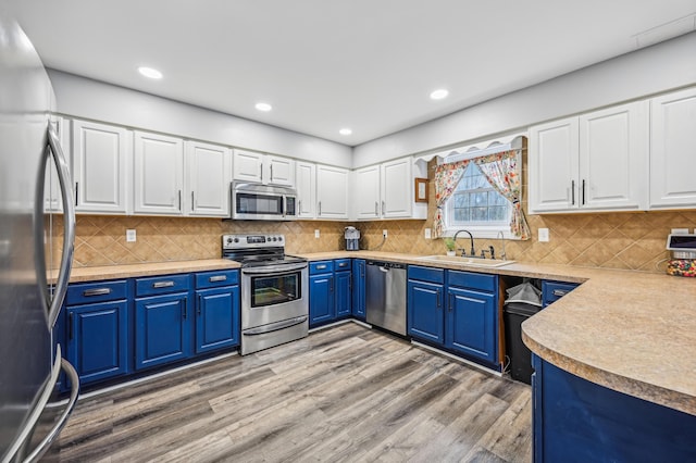 kitchen with sink, blue cabinets, appliances with stainless steel finishes, white cabinets, and light wood-type flooring