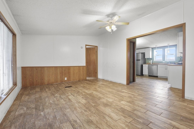 unfurnished room featuring ceiling fan, sink, light hardwood / wood-style flooring, wood walls, and a textured ceiling