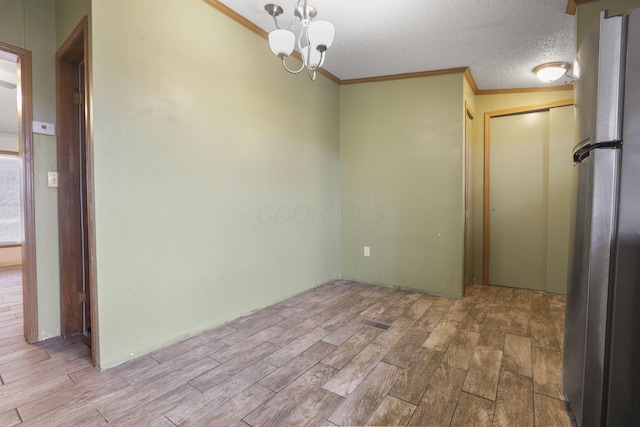 unfurnished room featuring an inviting chandelier, ornamental molding, a textured ceiling, and light hardwood / wood-style flooring