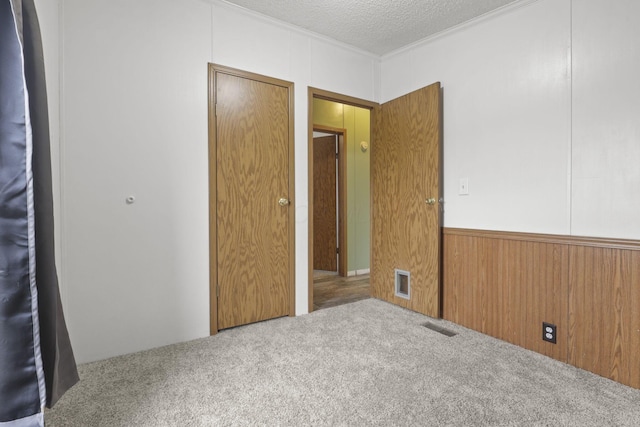 unfurnished bedroom with carpet flooring, ornamental molding, a textured ceiling, and wooden walls