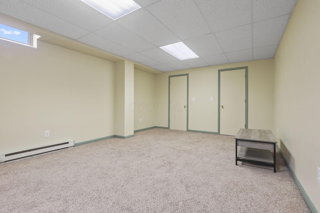 basement featuring light carpet, a paneled ceiling, and a baseboard heating unit