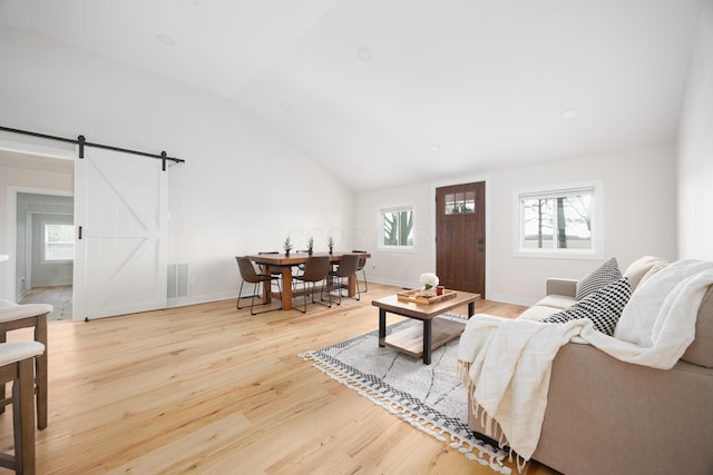 living room featuring light wood-type flooring, a barn door, and vaulted ceiling