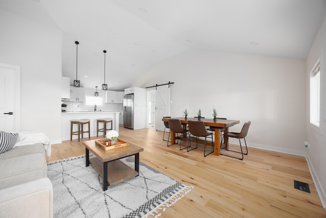 living room with light hardwood / wood-style floors, a barn door, sink, and high vaulted ceiling