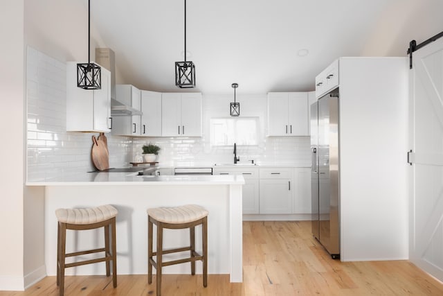 kitchen featuring sink, a barn door, backsplash, white cabinets, and light wood-type flooring