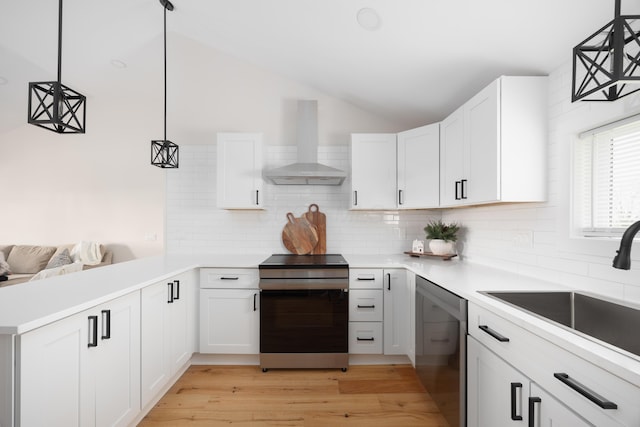 kitchen with decorative light fixtures, white cabinetry, stainless steel appliances, and wall chimney range hood