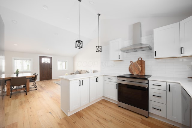 kitchen with pendant lighting, vaulted ceiling, wall chimney exhaust hood, and stainless steel range oven