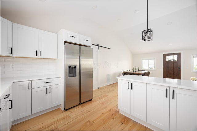 kitchen with pendant lighting, lofted ceiling, stainless steel fridge, a barn door, and white cabinetry