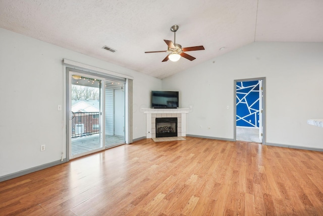 unfurnished living room featuring light wood-type flooring, a textured ceiling, vaulted ceiling, ceiling fan, and a tiled fireplace