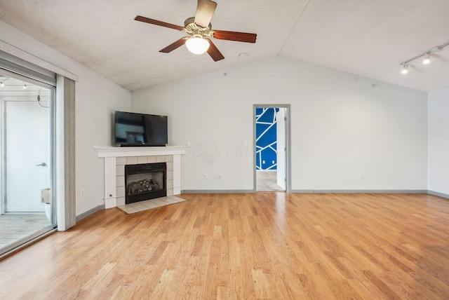 unfurnished living room featuring ceiling fan, a textured ceiling, vaulted ceiling, a tiled fireplace, and light wood-type flooring