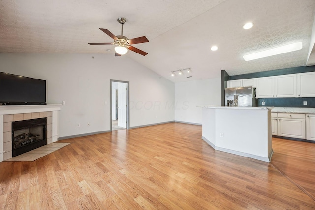 unfurnished living room featuring a tile fireplace, ceiling fan, light hardwood / wood-style flooring, a textured ceiling, and lofted ceiling