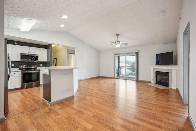 kitchen with stainless steel appliances, light hardwood / wood-style floors, vaulted ceiling, a fireplace, and white cabinets