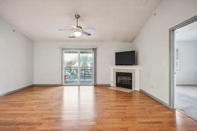 unfurnished living room featuring lofted ceiling, ceiling fan, a textured ceiling, light hardwood / wood-style floors, and a tiled fireplace