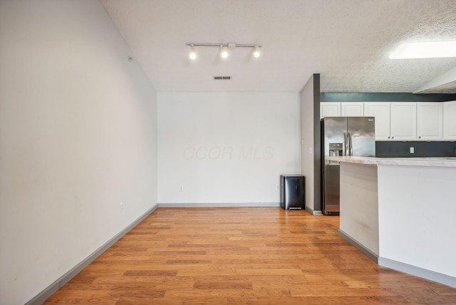 kitchen with stainless steel refrigerator with ice dispenser, vaulted ceiling, light hardwood / wood-style flooring, a textured ceiling, and white cabinetry