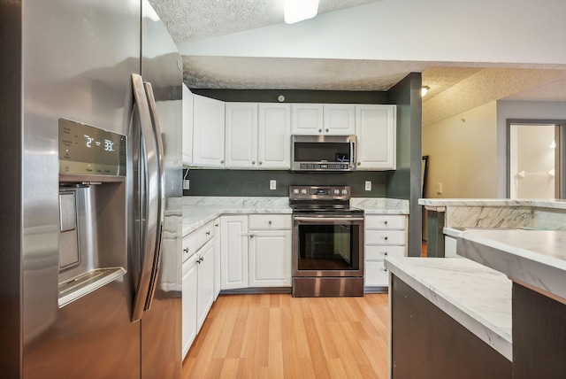 kitchen with white cabinetry, stainless steel appliances, light hardwood / wood-style floors, a textured ceiling, and vaulted ceiling