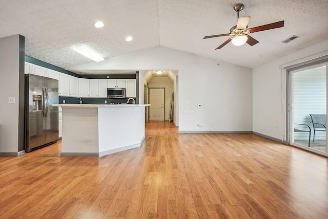 kitchen with a textured ceiling, stainless steel appliances, vaulted ceiling, light hardwood / wood-style flooring, and white cabinets