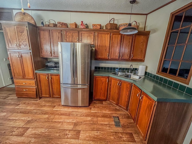 kitchen with sink, light wood-type flooring, a textured ceiling, decorative light fixtures, and stainless steel refrigerator