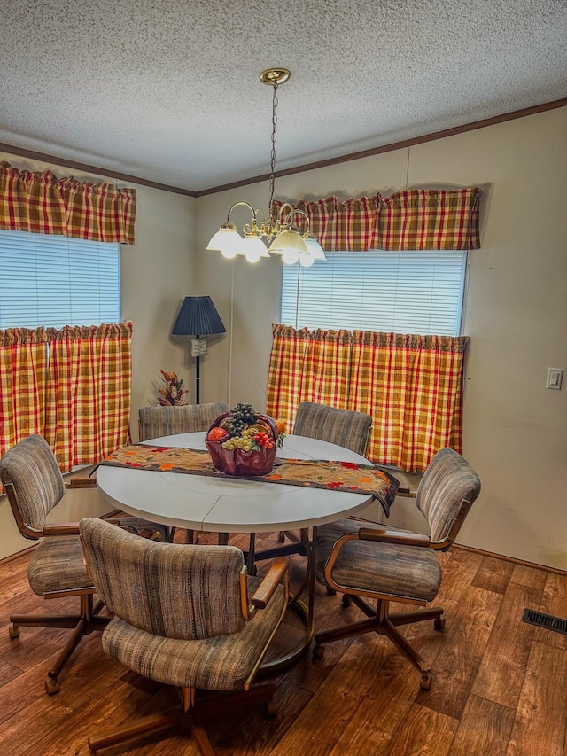 dining area featuring a notable chandelier, hardwood / wood-style floors, a textured ceiling, and ornamental molding