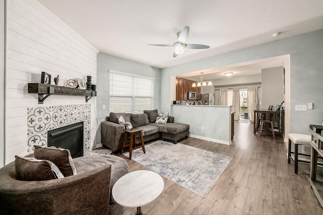 living room with ceiling fan with notable chandelier, a healthy amount of sunlight, dark wood-type flooring, and a tile fireplace