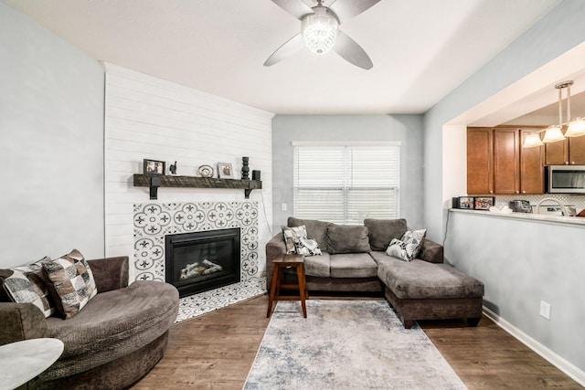 living room featuring a tile fireplace, ceiling fan, and dark wood-type flooring