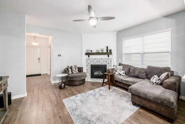 living room featuring wood-type flooring, ceiling fan, and a tiled fireplace