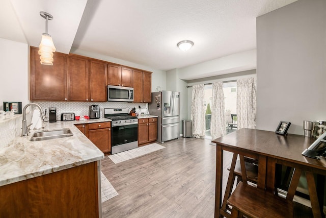 kitchen featuring sink, decorative backsplash, light wood-type flooring, appliances with stainless steel finishes, and decorative light fixtures