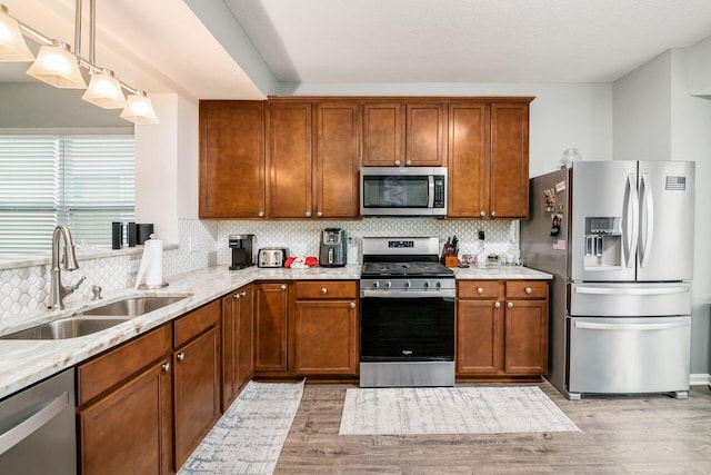 kitchen with sink, hanging light fixtures, stainless steel appliances, backsplash, and light hardwood / wood-style floors