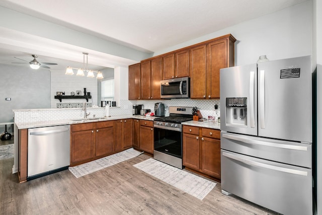 kitchen with sink, kitchen peninsula, light hardwood / wood-style floors, decorative light fixtures, and appliances with stainless steel finishes