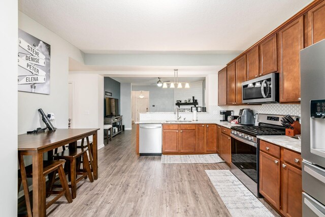 kitchen with decorative backsplash, appliances with stainless steel finishes, kitchen peninsula, decorative light fixtures, and light hardwood / wood-style flooring