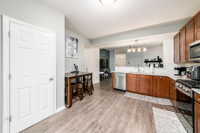 kitchen with sink, stainless steel appliances, backsplash, decorative light fixtures, and light wood-type flooring