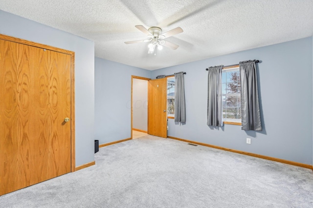 unfurnished bedroom featuring light carpet, a textured ceiling, a closet, and ceiling fan