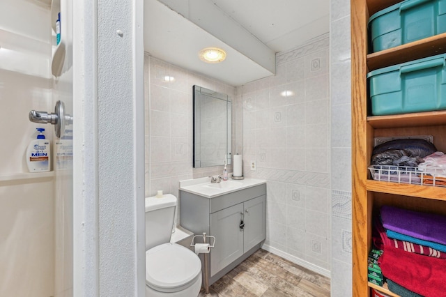 bathroom featuring vanity, toilet, wood-type flooring, and tile walls