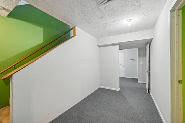 corridor featuring dark colored carpet and a textured ceiling