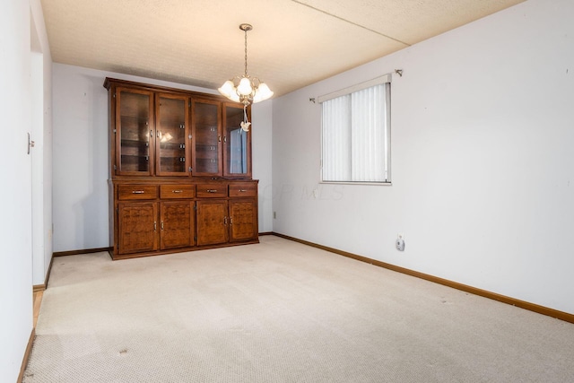 unfurnished dining area with a textured ceiling, light carpet, and an inviting chandelier