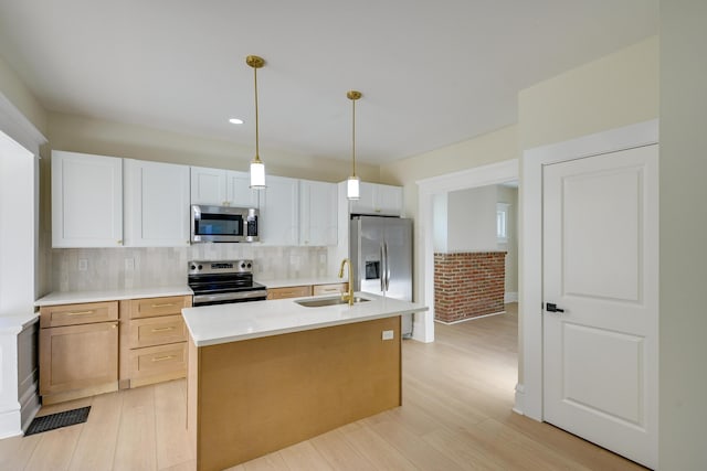 kitchen with sink, light wood-type flooring, an island with sink, appliances with stainless steel finishes, and white cabinetry